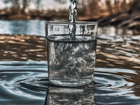 Water pouring into a clear glass surrounded by ripples, with a blurred natural background of trees and brown hues, creating a serene mood.